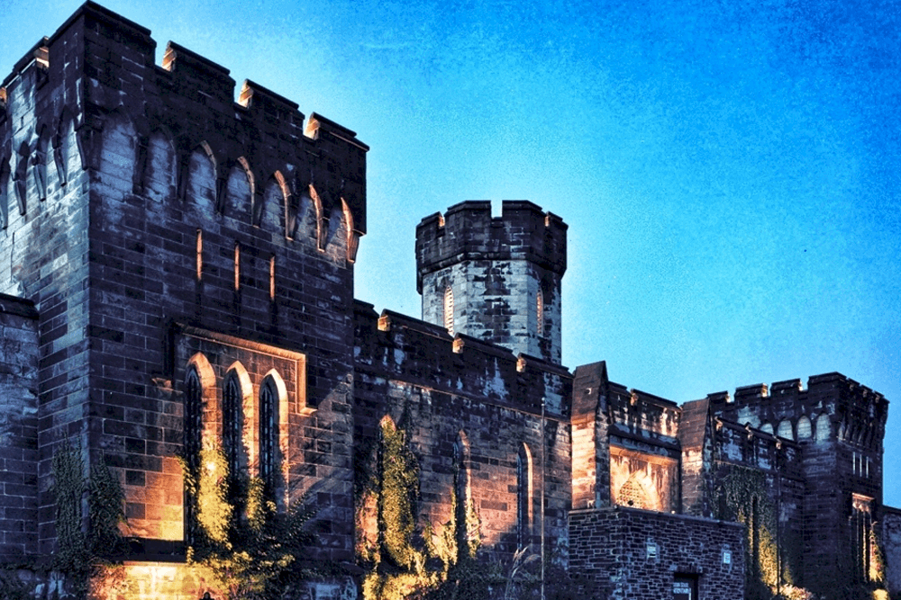Historic stone castle with turrets illuminated at dusk against a bright blue sky.