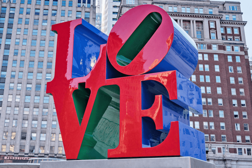 Colorful sculpture spelling "LOVE" in red, blue, and green against a city backdrop.