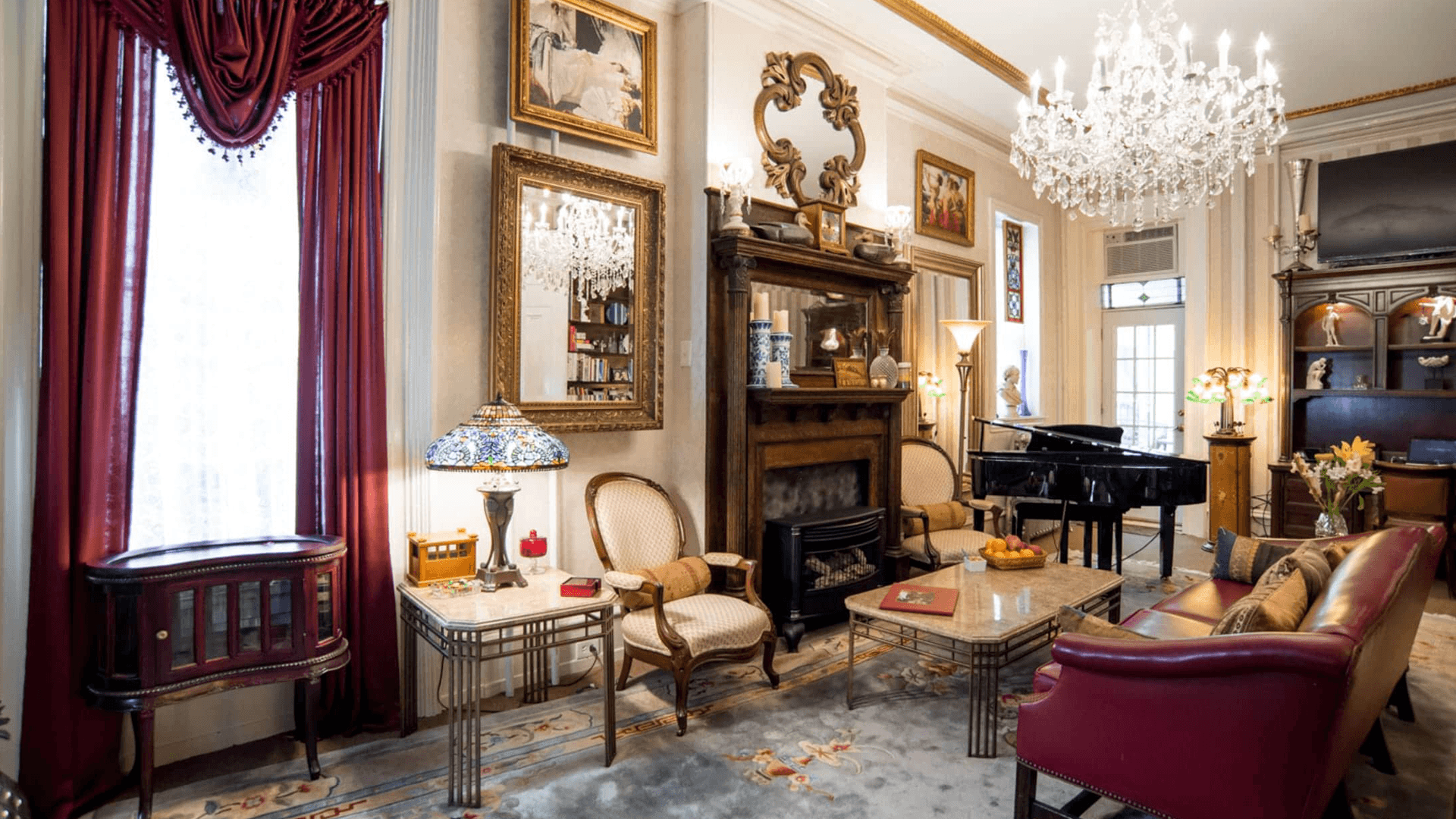 A stylish, elegantly decorated living room featuring vintage furniture, a grand piano, and a chandelier.