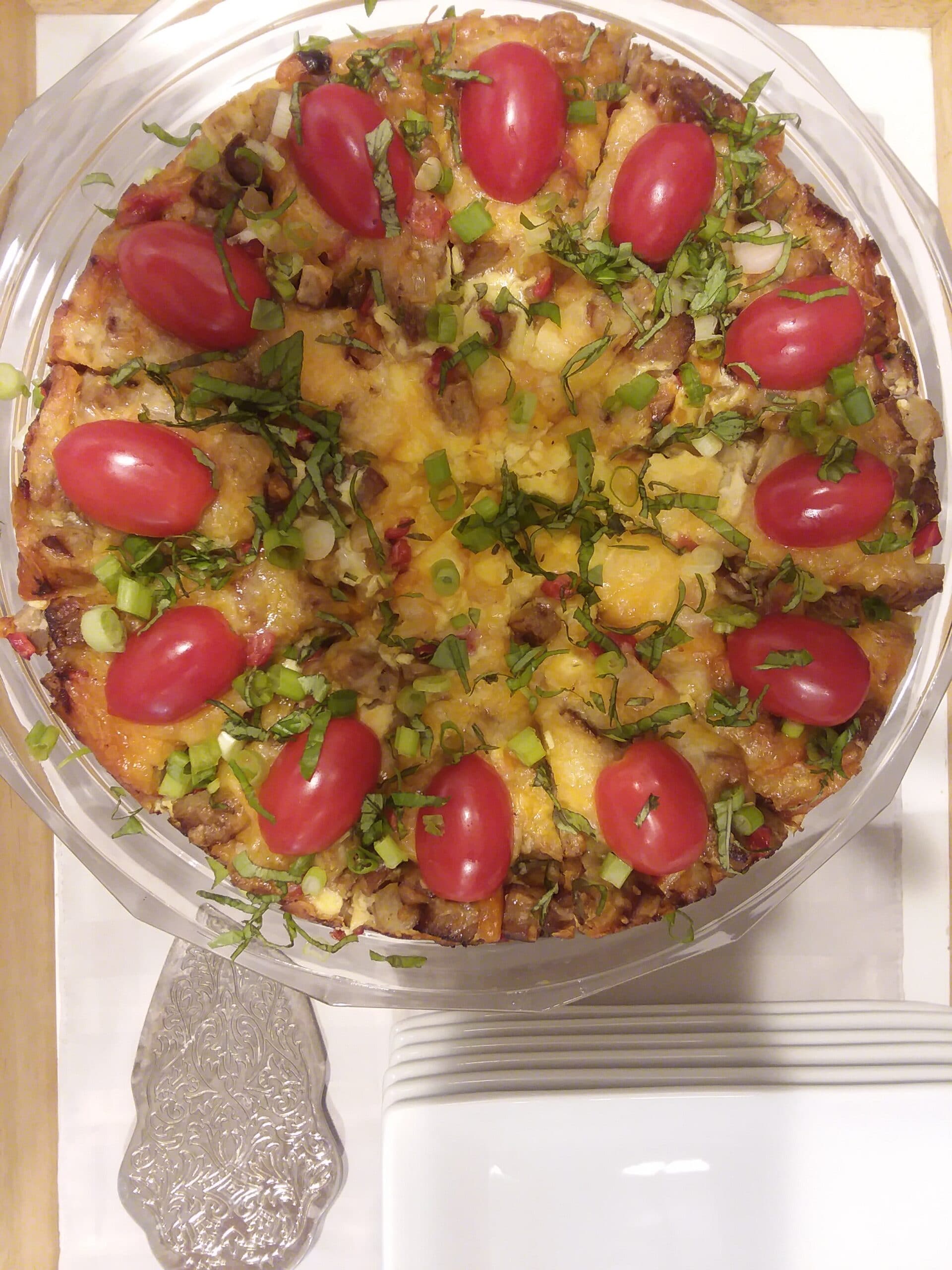 A colorful savory pie topped with cherry tomatoes, green onions, and fresh herbs.