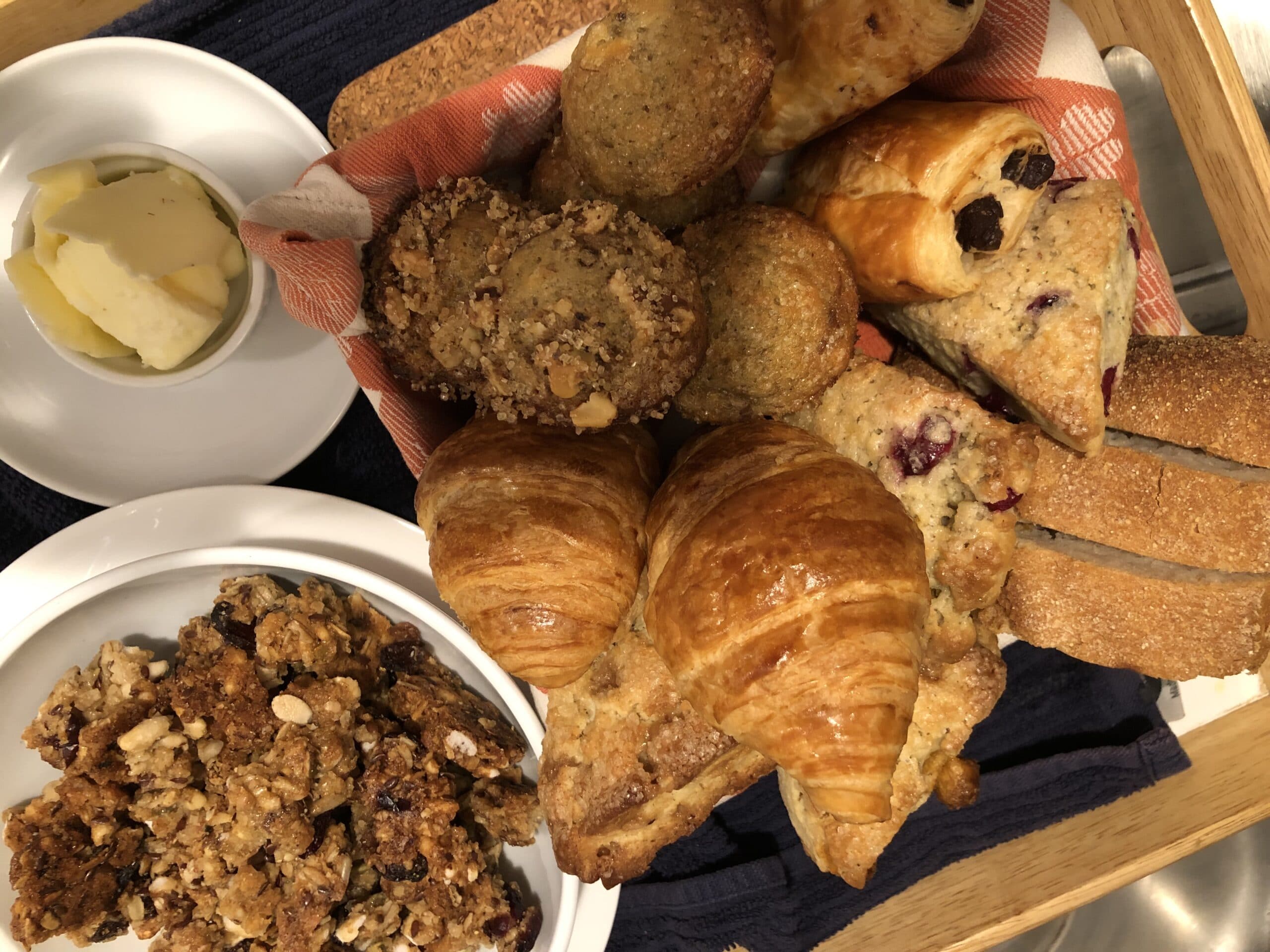 An assortment of baked goods including croissants, muffins, and granola, served with a small dish of butter.