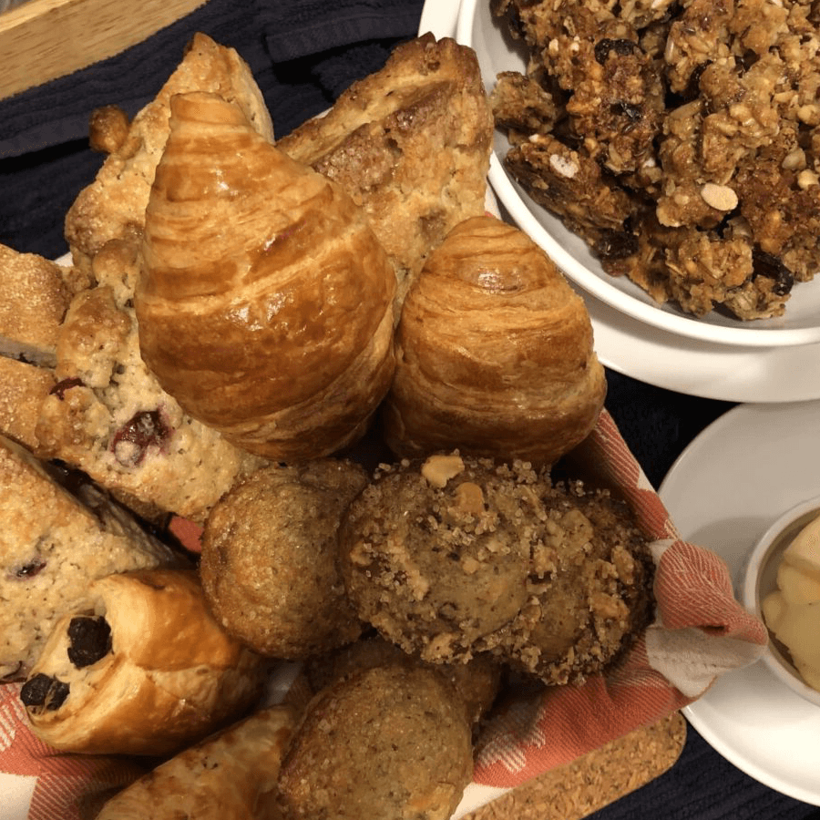 A variety of baked goods including croissants, muffins, and granola in a serving basket.