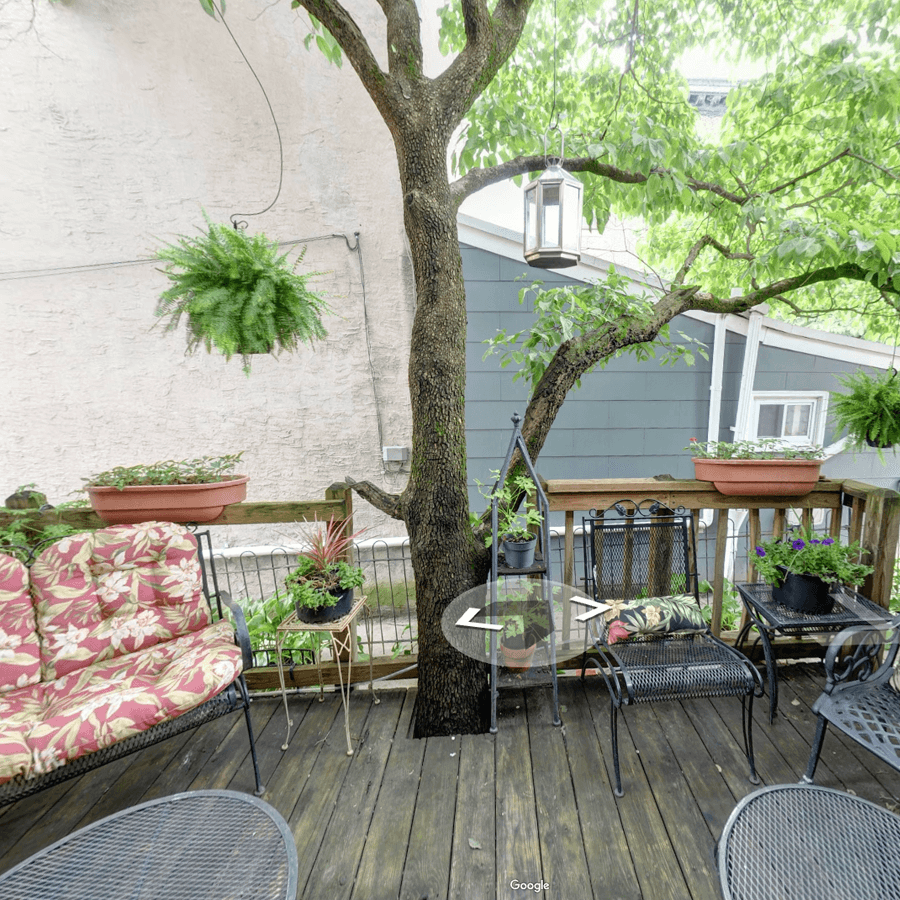 A cozy outdoor patio with potted plants, a large tree, and comfortable seating.