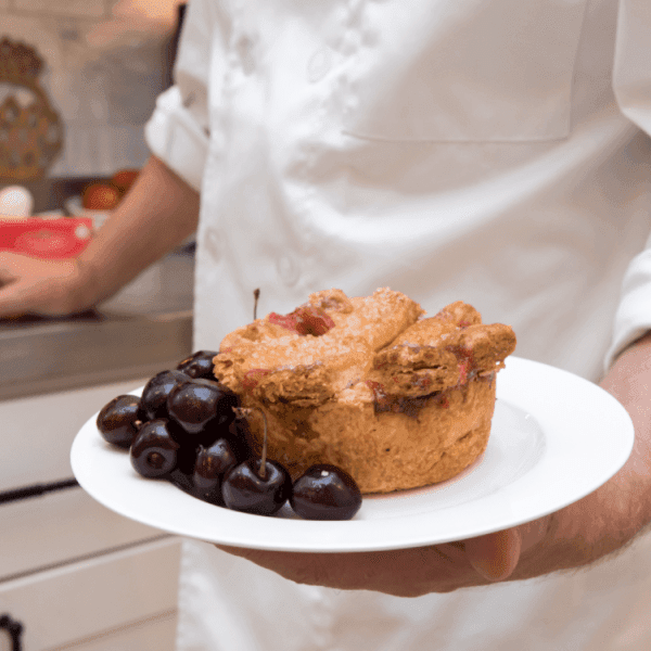 A chef holds a plate with a baked tart and fresh cherries.