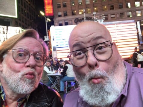 Two men with beards making playful pouty faces in Times Square at night.